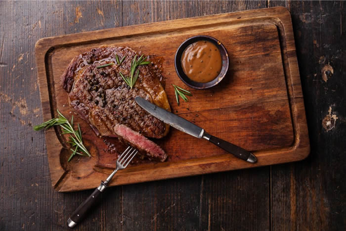 Gebakken vlees op plank met mes en vork en saus